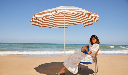 Woman sitting on a beach chair under an umbrella.