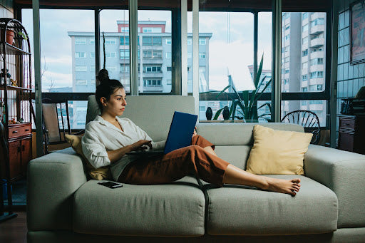 Woman typing on laptop sitting on couch.