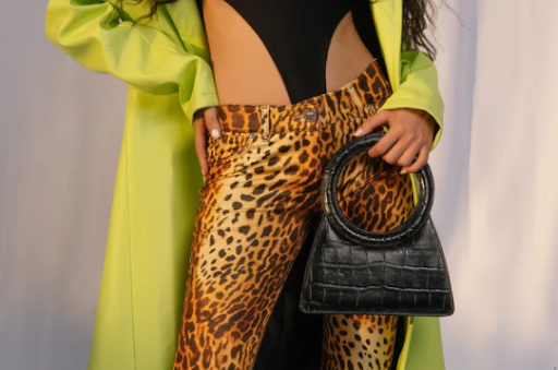 Woman wearing leopard pants holding a black purse.